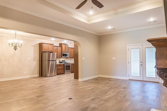 unfurnished living room featuring french doors, ceiling fan with notable chandelier, a tray ceiling, crown molding, and light hardwood / wood-style floors