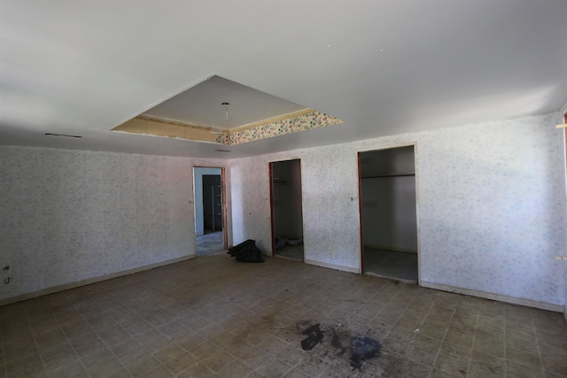 unfurnished bedroom with a tray ceiling, multiple closets, and wallpapered walls