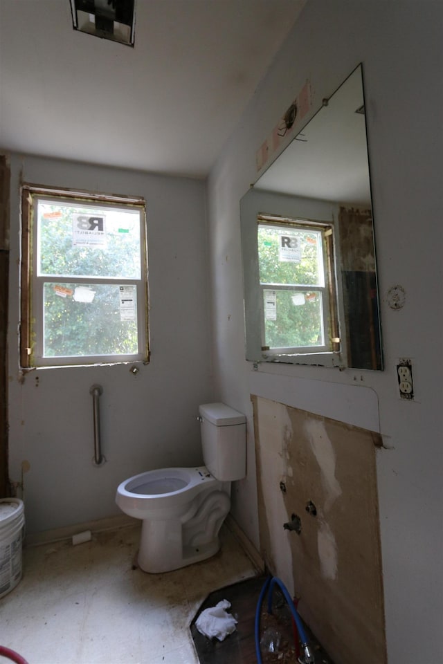 bathroom featuring toilet, a healthy amount of sunlight, and baseboards