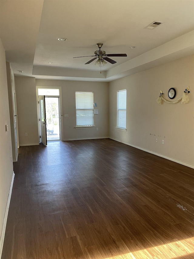 empty room with dark hardwood / wood-style floors, a raised ceiling, and ceiling fan