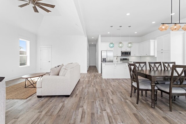 dining area featuring ceiling fan, lofted ceiling, sink, and light wood-type flooring