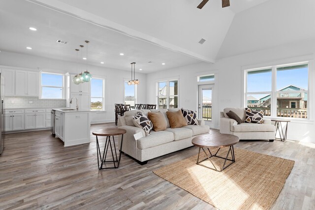 living room featuring ceiling fan with notable chandelier, high vaulted ceiling, sink, and light wood-type flooring