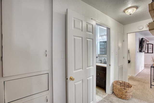 hallway with a textured ceiling, a sink, and light carpet