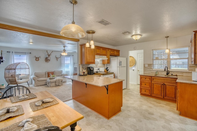 kitchen with under cabinet range hood, a sink, a kitchen breakfast bar, freestanding refrigerator, and a peninsula