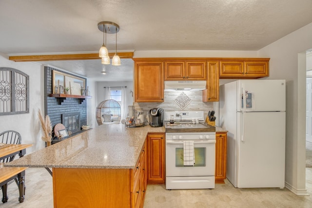 kitchen with brown cabinets, under cabinet range hood, white appliances, a peninsula, and a fireplace