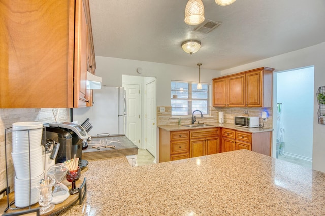 kitchen featuring visible vents, backsplash, brown cabinets, white appliances, and a sink