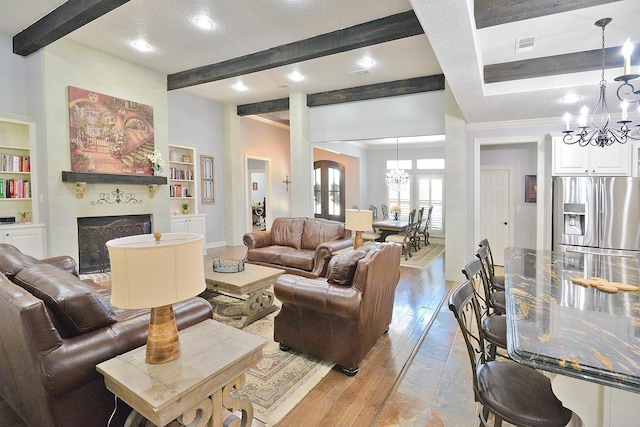 living area featuring a chandelier, beamed ceiling, light wood-style flooring, and a fireplace