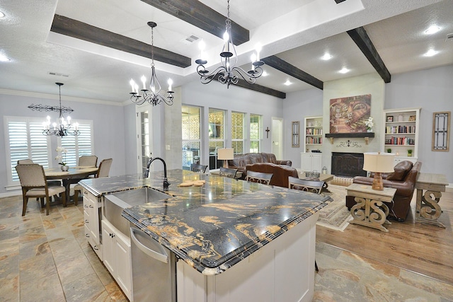 kitchen featuring beam ceiling, a fireplace, a kitchen island with sink, a sink, and stainless steel dishwasher