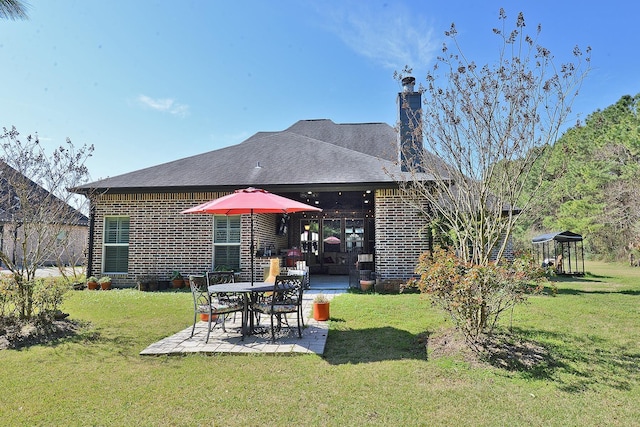 rear view of house featuring brick siding, roof with shingles, a lawn, a chimney, and a patio