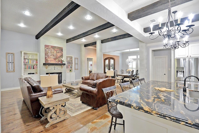 living area featuring an inviting chandelier, beamed ceiling, a fireplace, and light wood-style floors