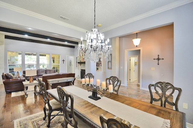 dining space featuring wood finished floors, visible vents, ornamental molding, a textured ceiling, and beamed ceiling