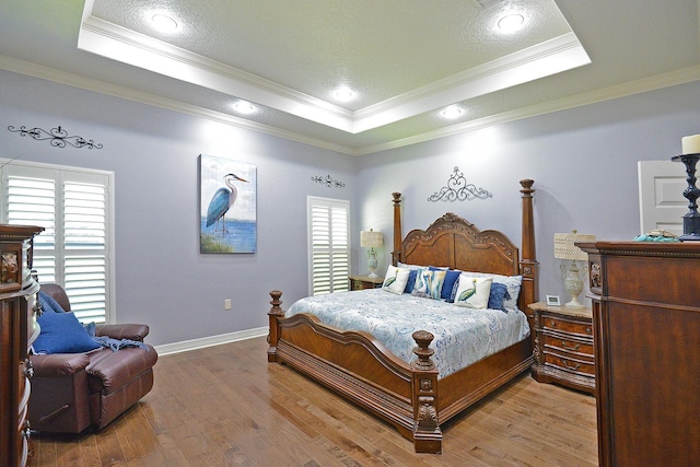 bedroom with a tray ceiling, baseboards, wood finished floors, and crown molding