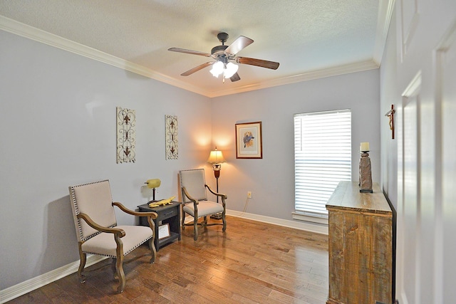 living area featuring ceiling fan, baseboards, ornamental molding, hardwood / wood-style flooring, and a textured ceiling