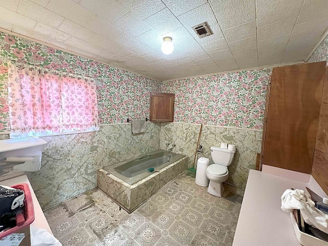 full bath featuring wallpapered walls, visible vents, wainscoting, toilet, and a bath