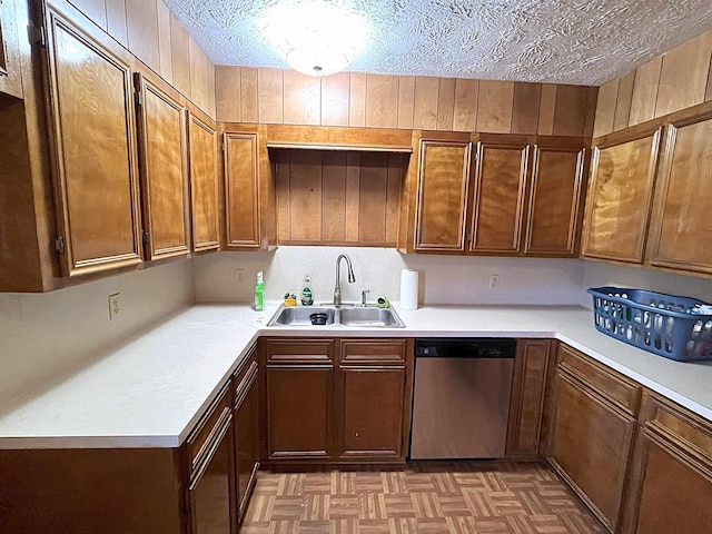 kitchen featuring brown cabinetry, light countertops, a textured ceiling, stainless steel dishwasher, and a sink