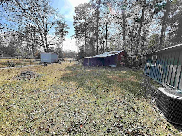 view of yard featuring a shed, central AC unit, an outdoor structure, and fence