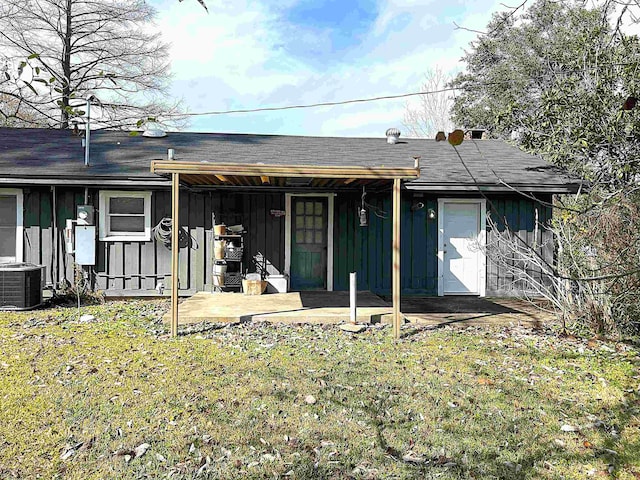 rear view of house featuring board and batten siding, a patio area, a lawn, and central AC unit