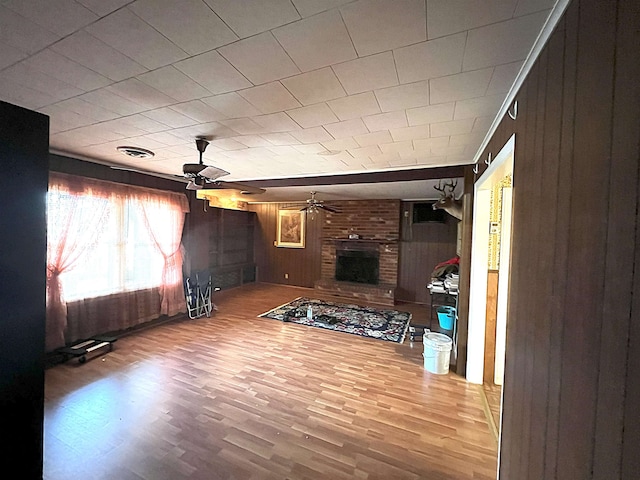 unfurnished living room with a brick fireplace, ceiling fan, wood finished floors, and wood walls