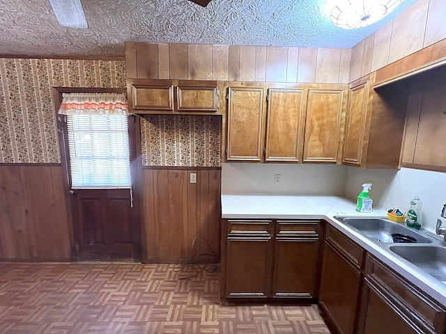 kitchen with a wainscoted wall, light countertops, wood walls, and a textured ceiling