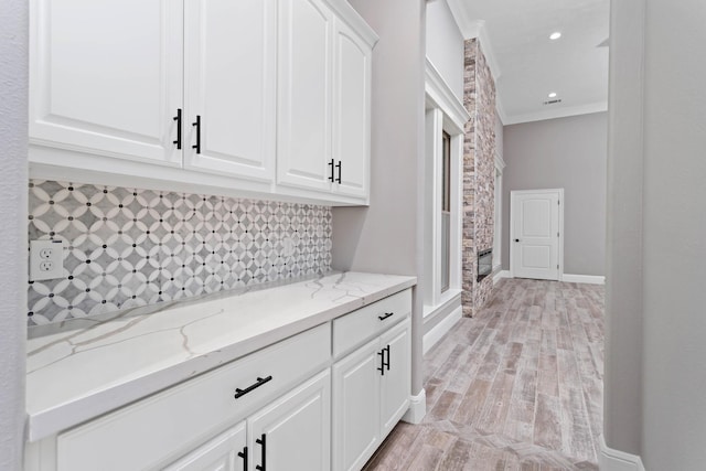 interior space with white cabinetry, decorative backsplash, ornamental molding, light stone counters, and light hardwood / wood-style flooring