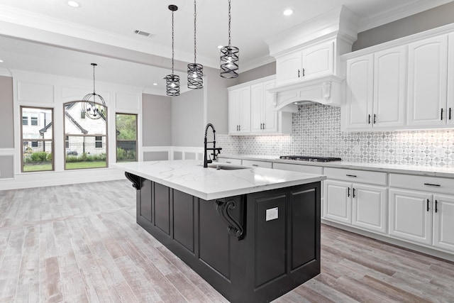 kitchen with light stone counters, a kitchen island with sink, sink, and white cabinets