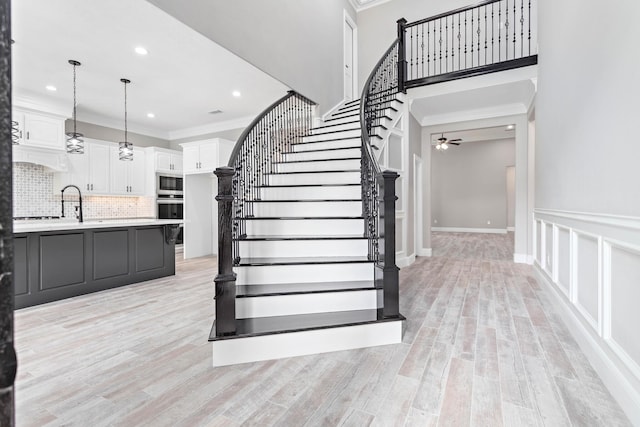 stairway with wood-type flooring, ornamental molding, and ceiling fan