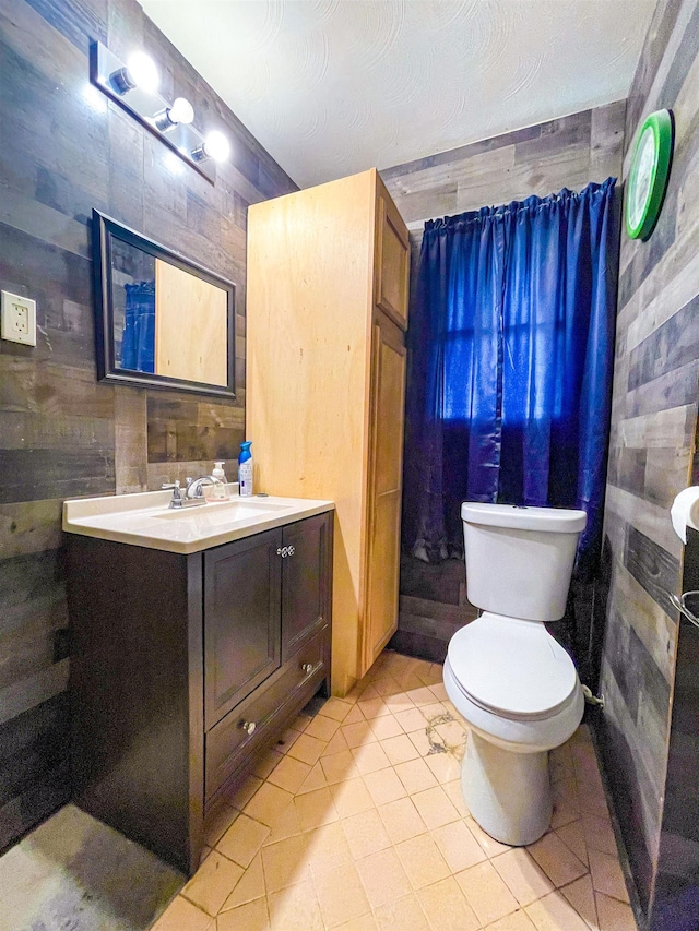 bathroom with vanity, tile patterned floors, wooden walls, toilet, and a textured ceiling