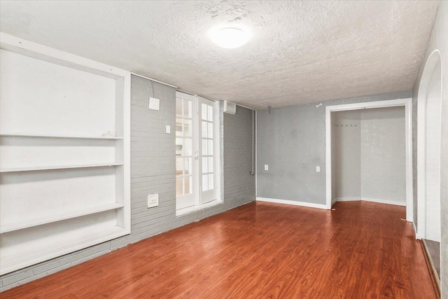 interior space with built in features, brick wall, dark wood-type flooring, and a textured ceiling