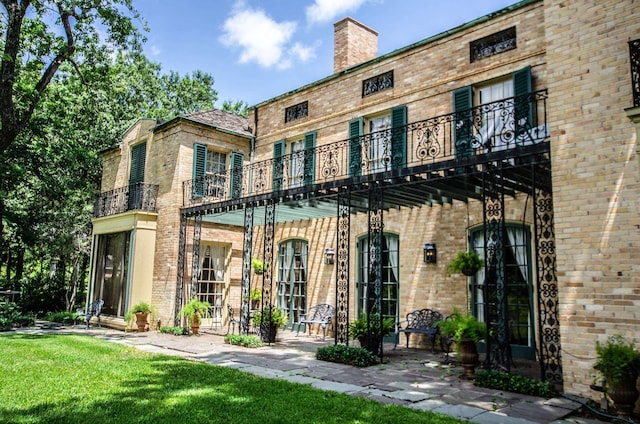 rear view of property with a balcony and a lawn