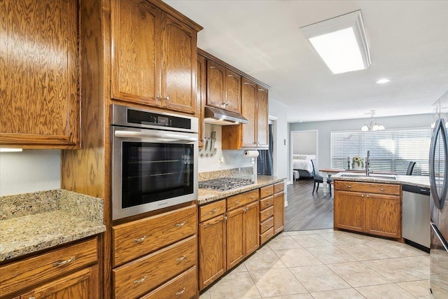 kitchen featuring sink, decorative light fixtures, appliances with stainless steel finishes, a notable chandelier, and light stone counters