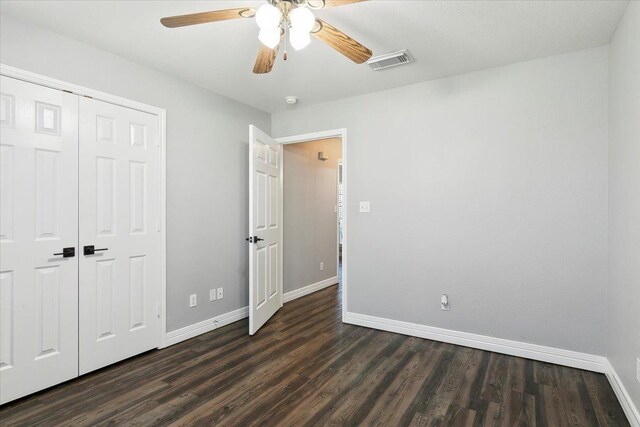 unfurnished bedroom with ceiling fan, a closet, and dark wood-type flooring