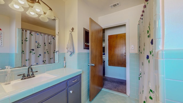 full bath featuring visible vents, a wainscoted wall, vanity, tile patterned floors, and tile walls