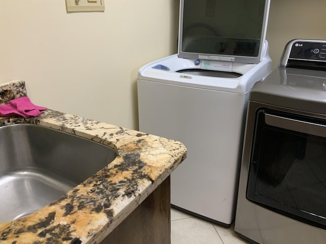 laundry area featuring washer and clothes dryer, sink, and light tile patterned floors