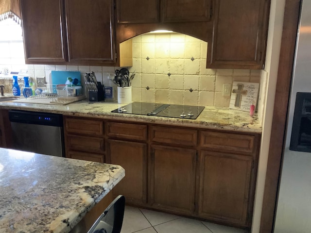 kitchen featuring backsplash, light stone counters, light tile patterned floors, and stainless steel appliances