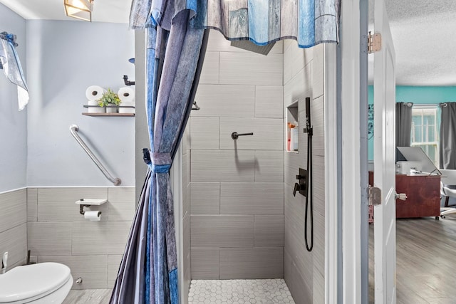 full bathroom featuring toilet, a wainscoted wall, wood finished floors, tile walls, and a tile shower