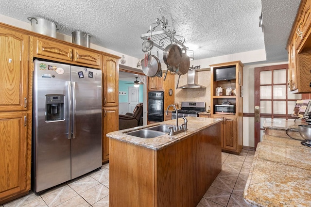 kitchen featuring light tile patterned flooring, a kitchen island with sink, stainless steel appliances, a sink, and wall chimney exhaust hood