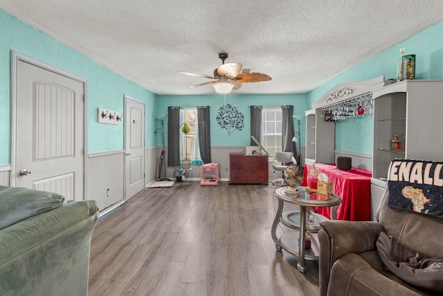 living area featuring a wainscoted wall, a textured ceiling, wood finished floors, and a ceiling fan