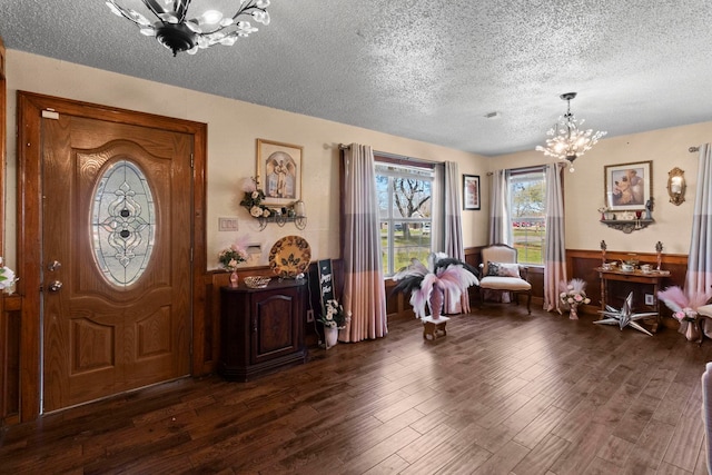 entryway with a chandelier, a wainscoted wall, a textured ceiling, and dark wood-type flooring