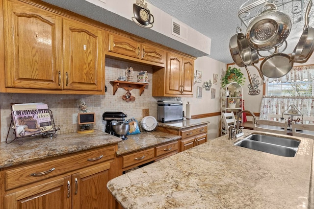 kitchen featuring visible vents, brown cabinetry, light stone countertops, a textured ceiling, and a sink