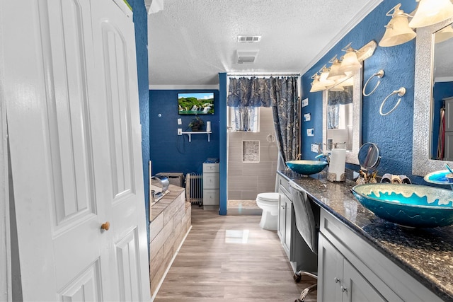 full bath featuring a textured ceiling, wood finished floors, a sink, visible vents, and double vanity