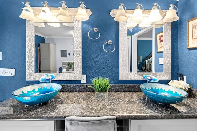 bathroom with a textured wall, crown molding, a sink, and double vanity