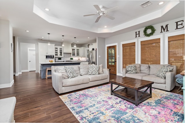 living room with ceiling fan, dark hardwood / wood-style flooring, a raised ceiling, and sink