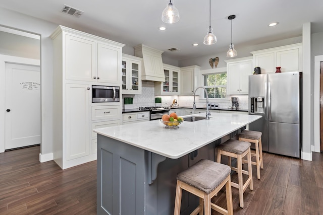 kitchen featuring appliances with stainless steel finishes, tasteful backsplash, white cabinetry, sink, and a center island with sink