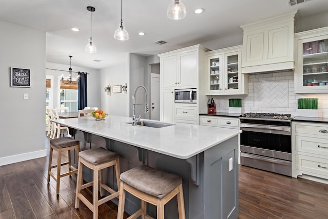 kitchen with hanging light fixtures, appliances with stainless steel finishes, sink, and a kitchen island with sink