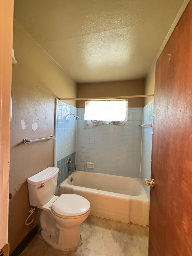 bathroom featuring a textured ceiling, toilet, and tiled shower / bath