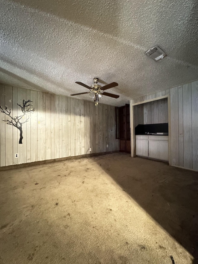 interior space with a textured ceiling, carpet floors, ceiling fan, and wooden walls