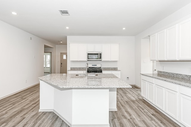 kitchen with a center island with sink, white cabinets, sink, light stone countertops, and stainless steel appliances