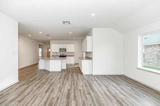 kitchen with white cabinetry, light hardwood / wood-style flooring, an island with sink, vaulted ceiling, and appliances with stainless steel finishes