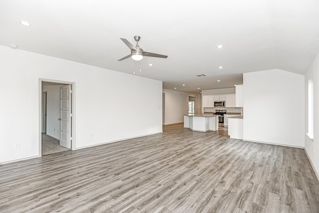 unfurnished living room with ceiling fan, light hardwood / wood-style flooring, vaulted ceiling, and sink