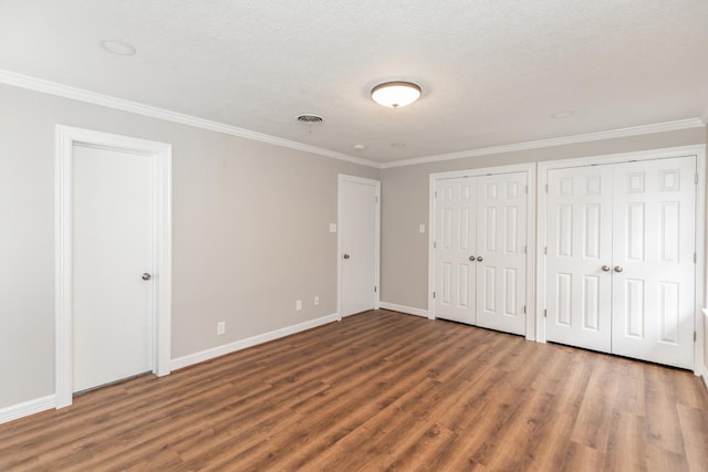 unfurnished bedroom featuring hardwood / wood-style floors, a textured ceiling, two closets, and crown molding